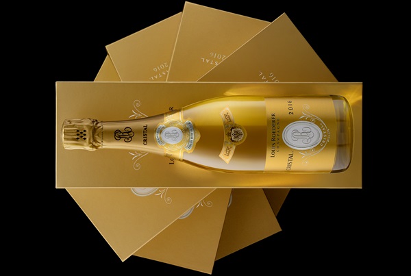 Eine Flasche Champagner steht auf einer goldenen Verpackung, umgeben von mehreren goldfarbenen Karten. Die Flasche zeigt das Jahr 2016 und trägt ein elegantes Design.