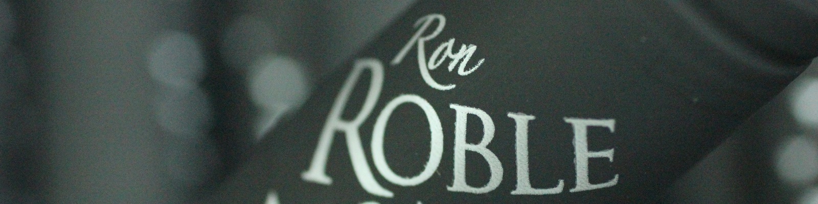 Ron Roble Ein schwarzes Flaschenetikett mit dem textuellen Schriftzug -Ron Roble-, auf einem verschwommenen Hintergrund. Das Etikett ist elegant und gut lesbar.