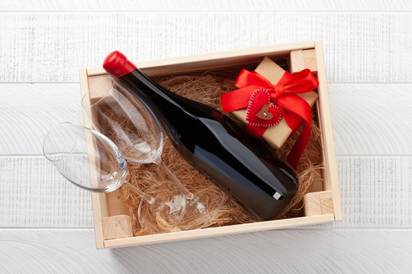 Eine Flasche Rotwein ist mit einem Jutesack und einem goldenen Schleifenband umwickelt und liegt auf einer rustikalen Holztischoberfläche.