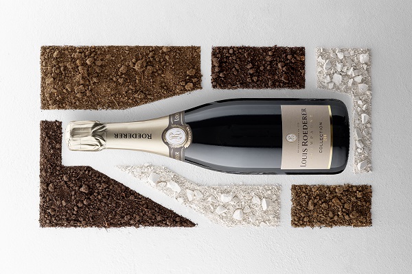 LR_COLLECTION 244 SURROUNDED WITH PLOTS_600x400 Eine Flasche Louis Roederer Champagner liegt auf einem weißen Untergrund, umgeben von verschiedenen Erdmischungen in Braun- und Grautönen, die ein grafisches Muster bilden.