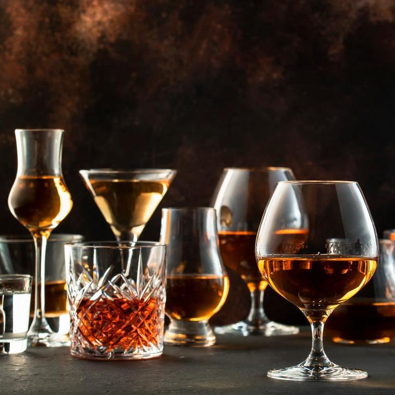 Eine Anordnung verschiedener Getränke in Gläsern, darunter Schnaps, Cocktails und Whisky, auf einer eleganten Oberfläche. Der Hintergrund ist dunkel und erzeugt eine stilvolle Atmosphäre.