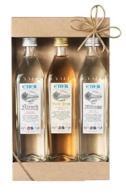 Geschenkbox Etter Minis Drei Flaschen Obstler stehen in einer Geschenkschachtel. Die Flaschen sind sorgfältig etikettiert und sichtbar, eine trägt die Aufschrift -Kirsche-, die andere -Alte Treue- und die letzte -William-. Der Karton ist mit einer Schleife dekoriert.