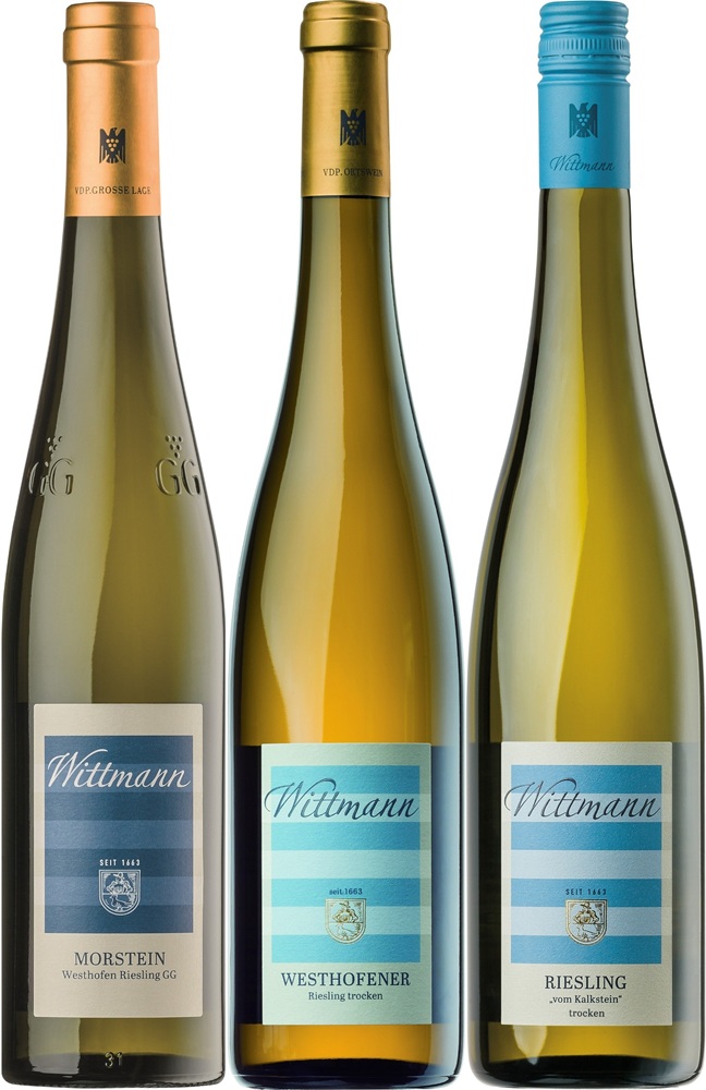 Drei Weinflaschen stehen nebeneinander. Die linke Flasche ist Morstein, die mittlere Westhofener und die rechte Riesling, alle mit unterschiedlichen Etiketten und Kapseln in Blau- und Goldtönen.