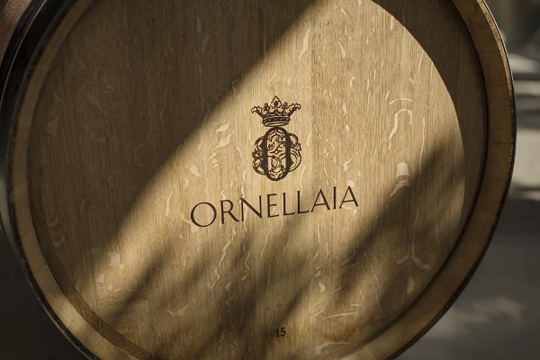 Ein Holzfass ist abgebildet, auf dem die Inschrift -ORNELLAIA- und ein Wappen mit einer Krone zu sehen sind. Schattenspiele fallen auf die Fassoberfläche.