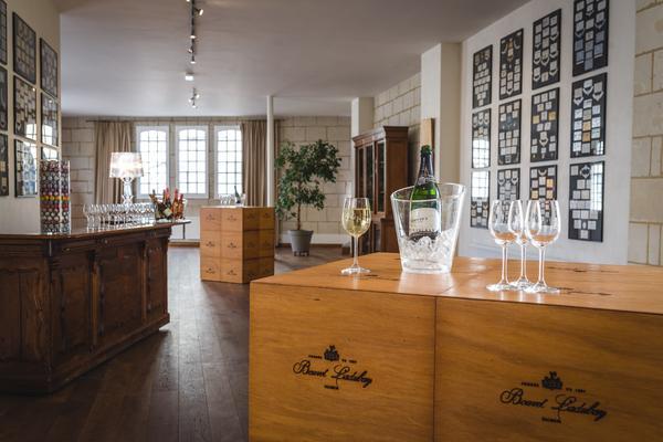 Holzkisten stehen in einem eleganten Raum mit Holzboden. Ein Glaskübel mit Champagner und Weingläsern sind auf einer Kiste platziert. Wände sind mit Kunstwerken und Auszeichnungen geschmückt.