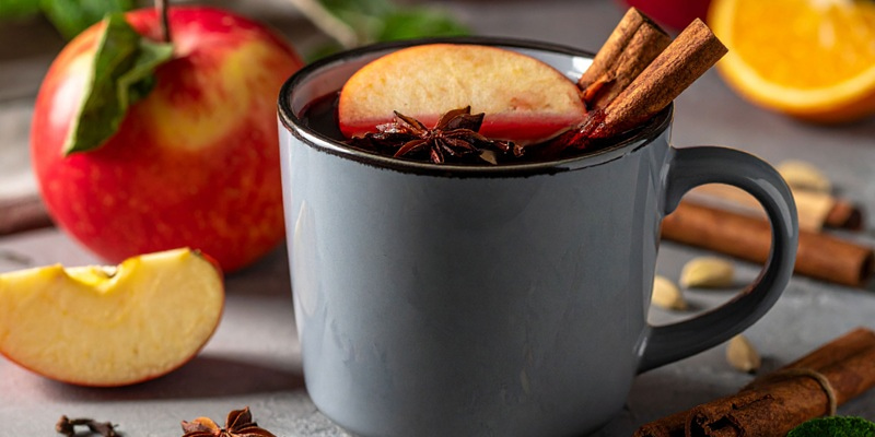 Zwei durchsichtige Gläser mit heißem Getränk, dekoriert mit Zimtstangen, Sternanis und Zitronenscheiben, stehen auf einem Holzbrett. Frische Rosmarinzweige ergänzen die servierte Präsentation.