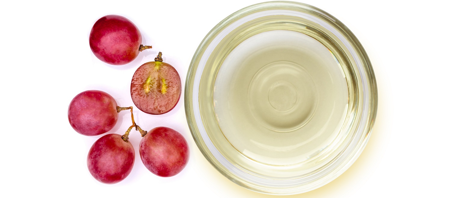 Die Welt der Blanc de Noir Weine Rote Trauben liegen neben einer kleinen Schale mit klarem, hellgelbem Öl. Einige der Trauben sind halbiert und zeigen das Innere.