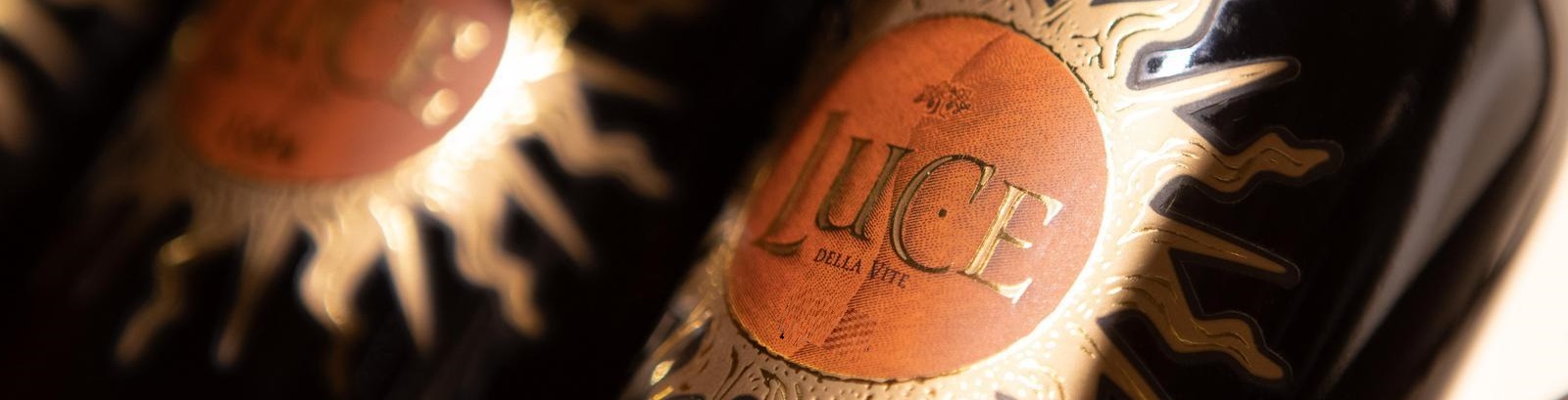 Dunkle Weinflaschen mit goldverziertem Etikett und der Aufschrift -Luce della Vite-. Die Flaschen sind unscharf im Hintergrund, betonen stilvolles Design und luxuriöse Ausstrahlung.