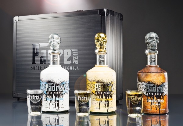 Drei Flaschen Tequila mit kunstvollen Totenschädel-Deckeln stehen in einer Reihe vor einer schwarzen Box. Vor den Flaschen stehen Gläser, die bereit zum Servieren sind.