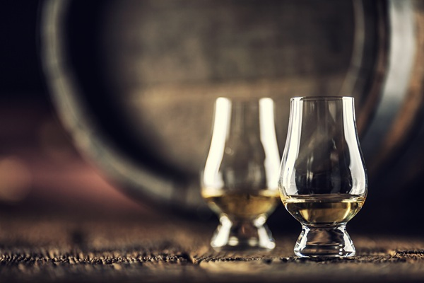 Zwei Gläser mit Whisky, in denen sich jeweils ein Eiswürfel befindet. Sie stehen auf einem rustikalen Holzuntergrund, umgeben von einer warmen, Holztextur.