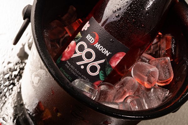 Eine Flasche -Red Moon 996- mit rotem Apfelgeschmack steht in einem Eisbehälter voller Eiswürfel. Der Behälter ist von Wassertröpfchen umgeben, was Frische vermittelt.