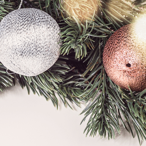 Silberne und bronze-farbene Weihnachtskugeln hängen an einer grünen Tannenzweigen. Die Kugeln haben unterschiedliche Texturen und sind Teil einer festlichen Dekoration.