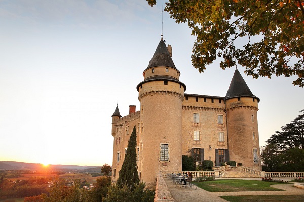 Ein prächtiges Schloss mit Türmen steht im Mittelpunkt, während die Sonne im Hintergrund aufgeht. Der Garten ist gepflegt und bietet eine Aussicht auf die umliegenden Landschaften.