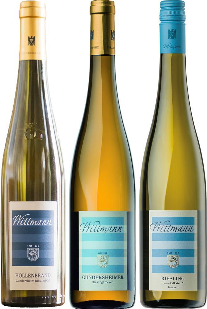 Drei Weinflaschen stehen nebeneinander. Jede Flasche hat ein Etikett mit verschiedenen Namen: Höllenbrand, Gundersheimer und Riesling. Die Flaschen haben unterschiedliche Farben und Verschlüsse.