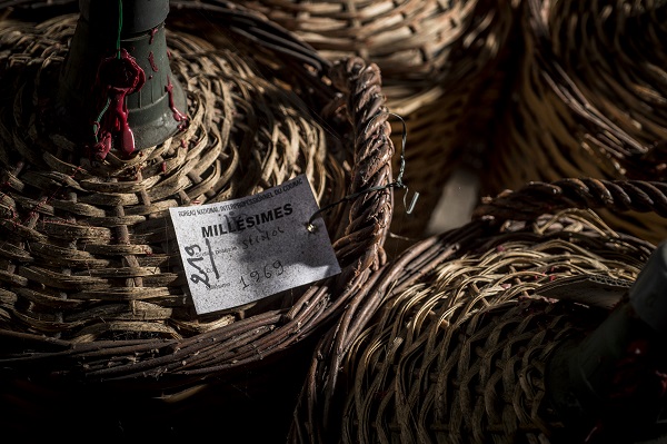 Korb mit einem etikettierten Tag, der -MILLÉSIMES- und -1969- zeigt, liegt zwischen mehreren weiteren geflochtenen Körben in einem schattigen Raum.