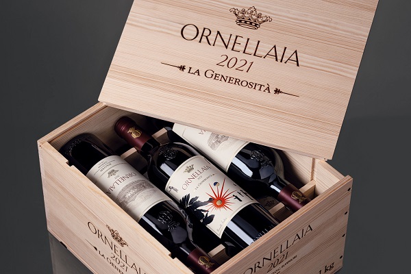 Ornellaia_Kiste_2021_600 Holzkiste mit offenem Deckel, darin drei Weinflaschen mit verschiedenen Etiketten. Die Kiste trägt die Aufschrift -ORNELLAIA 2021 LA GENEROSITÀ-. Sie steht auf einer reflektierenden Oberfläche.