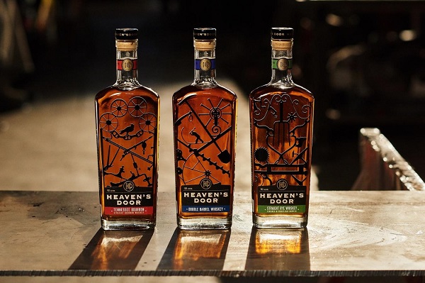 Drei Flaschen Whiskey stehen auf einem Tisch. Die Flaschen sind mit kunstvollen Etiketten versehen, die verschiedene Symbole zeigen. Das Licht betont die Farbe des Whiskeys im Inneren.