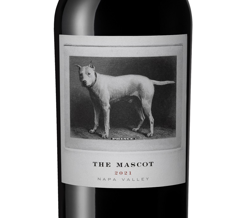 Eine Weinflasche mit etiket, das einen Hund zeigt. Der Hund steht auf einem klassischen, monochromen Hintergrund. Der Etikettentext lautet: -THE MASCOT 2021 NAPA VALLEY-.
