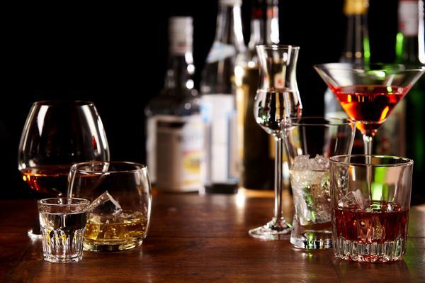 Auf einem Tisch stehen verschiedene Gläser mit alkoholischen Getränken, darunter Cocktails und Spirituosen. Im Hintergrund sind mehrere Flaschen sichtbar, während die Beleuchtung eine gemütliche Atmosphäre schafft.