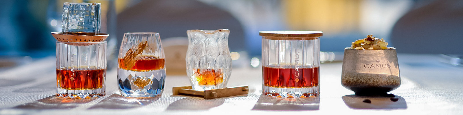 Camus Fünf stilvolle Gläser mit unterschiedlichen Spirituosen und ansprechendem Design stehen auf einem eleganten Tisch. Der Hintergrund ist verschwommen und lässt eine festliche Atmosphäre erahnen.