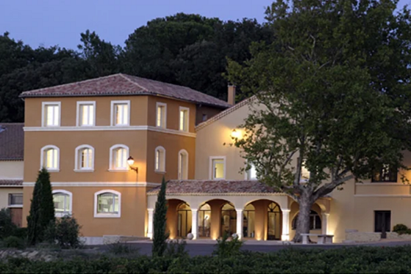 Ein elegantes Gebäude mit zwei Stockwerken, beleuchtet von warmem Licht, steht im Vordergrund. Umgeben von Bäumen und einer grünen Umgebung, vermittelt es eine ruhige Atmosphäre.