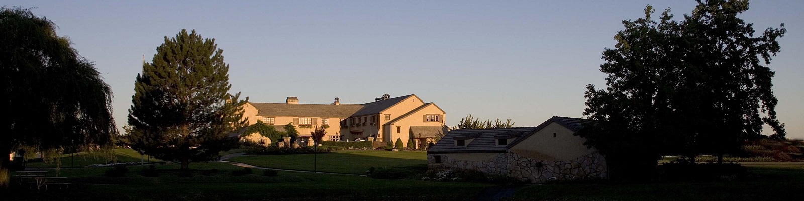 Columbia Crest Ein großes, mehrstöckiges Gebäude mit einem gewölbten Dach steht im Vordergrund, umgeben von einem gepflegten Grünbereich und hohen Bäumen, unter einem klaren Abendhimmel.