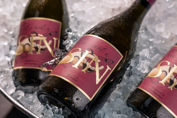 Drei Flaschen Wein liegen auf Eis in einer silbernen Schüssel. Die Flaschen haben ein elegantes, burgunderfarbenes Etikett mit dem Schriftzug -Not a Sin-.