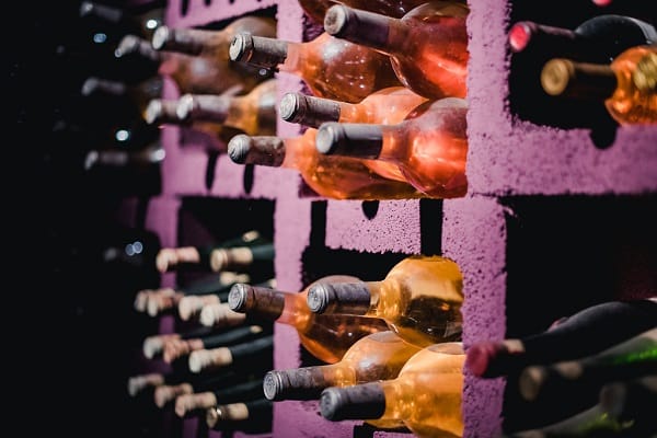 Flaschen unterschiedlichen Weins stehen in einem lila Regal. Einige Glasflaschen sind roséfarben, während andere grün und braun sind. Die Flaschen sind ordentlich angeordnet und teilweise sichtbar.