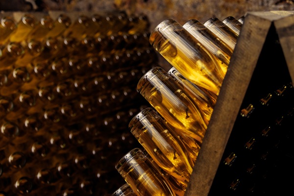 Eine Gruppe flacher, goldener Flaschen ist eng angeordnet. Die Flaschen stehen senkrecht auf einem dunklen Untergrund, wobei ihre Oberseiten glänzen und Reflexionen zeigen.