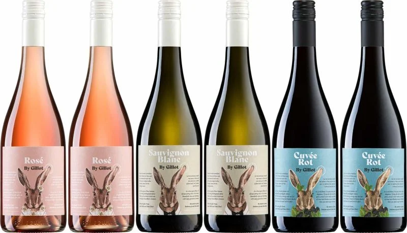 Sechs Weinflaschen stehen nebeneinander. Links zwei Flaschen Rosé, gefolgt von zwei Flaschen Sauvignon Blanc und rechts zwei Flaschen Cuvée Rot. Jede Flasche hat ein etiket mit einem Hasenmotiv.