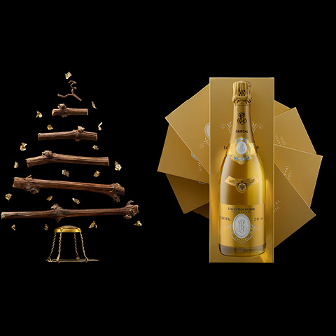 Ein dekorativer Baum aus Ästen steht links, umgeben von goldenen Elementen. Rechts ist eine stilisierte, goldene Champagnerflasche in einer eleganten Verpackung, neben ihr liegen mehrere goldene Umschläge.