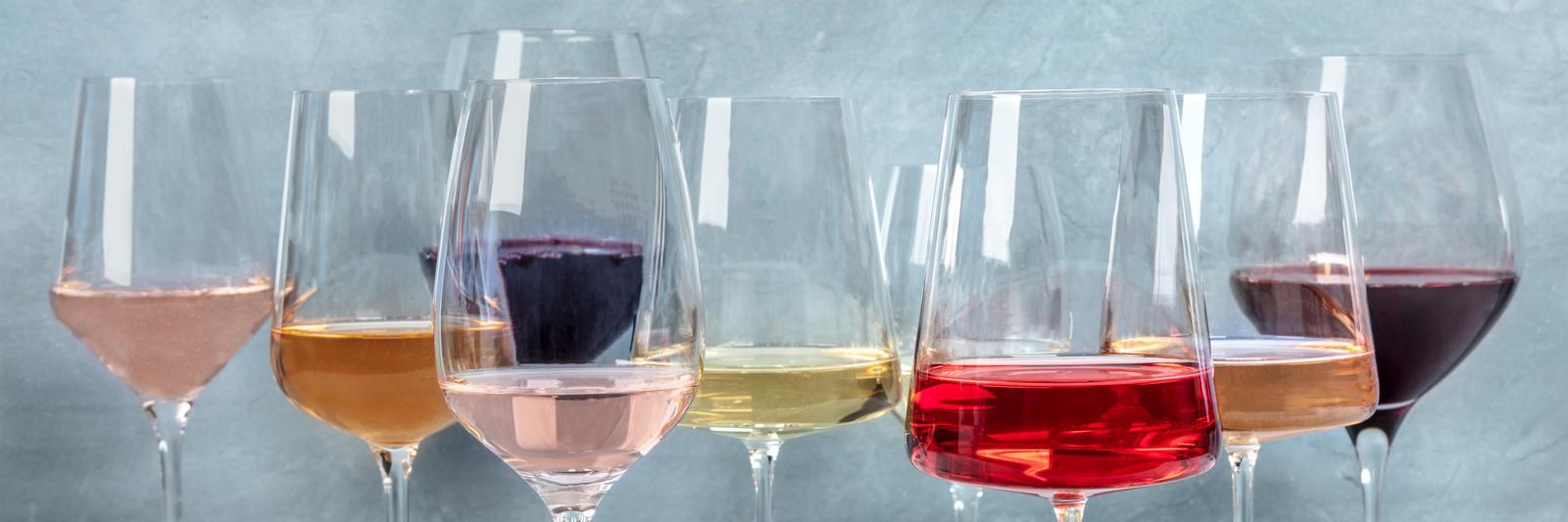 Mehrere Weingläser mit verschiedenen Getränken, darunter rosé, rot, weiß und orange, stehen hintereinander vor einem hellblauen Hintergrund.