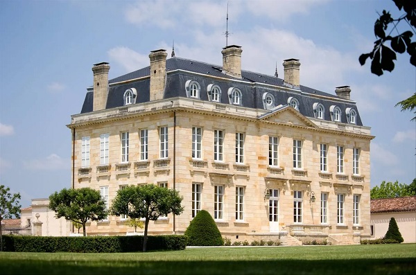 Ein stattliches, historisches Gebäude mit mehreren Etagen und großen Fenstern, umgeben von gepflegten Gärten und Bäumen, unter einem klaren blauen Himmel.