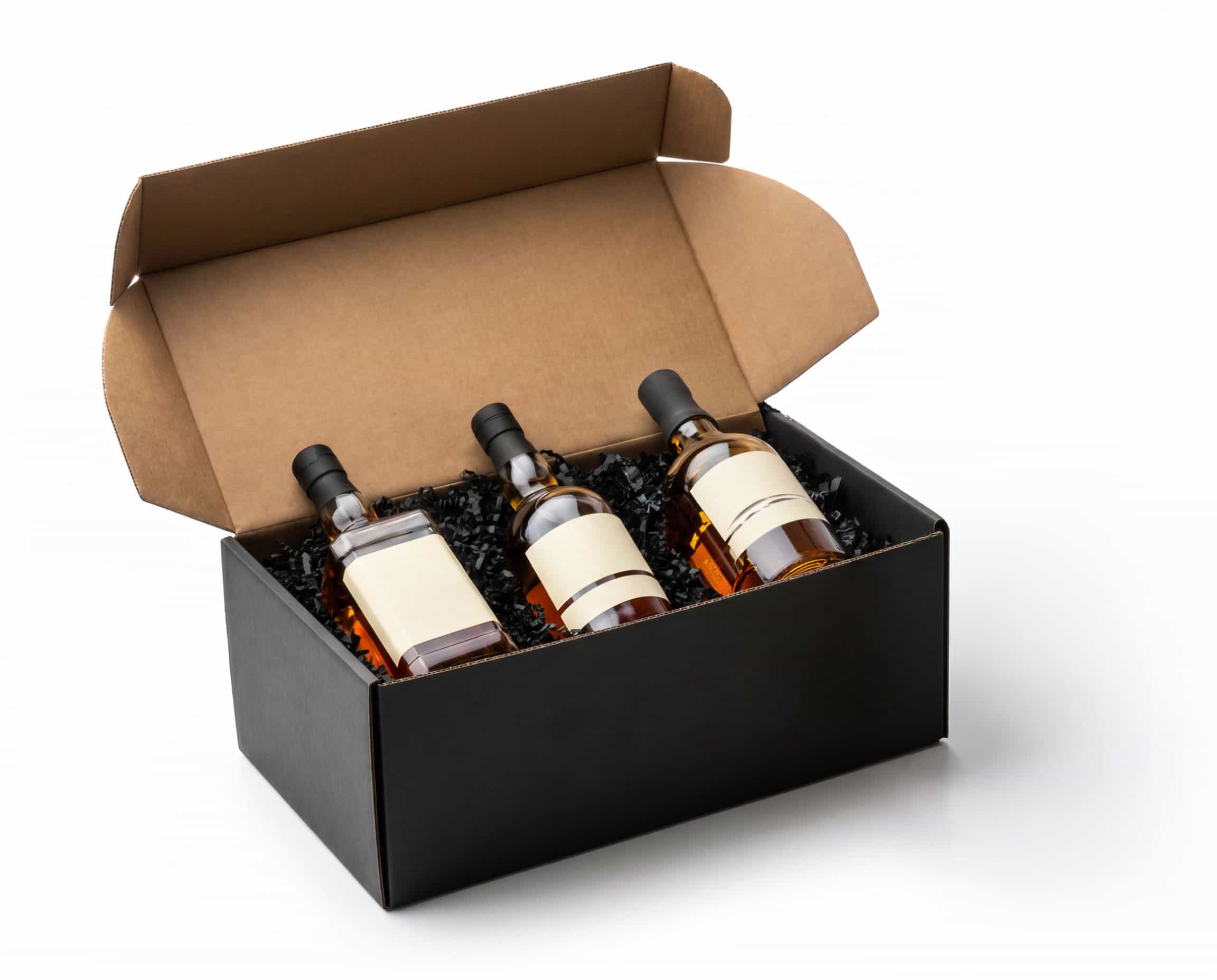 Drei Flaschen mit alkoholischem Inhalt liegen in einem offenen schwarzen Geschenkkarton. Der Karton enthält schwarzes Füllmaterial und hat einen hellen, neutralen Hintergrund.