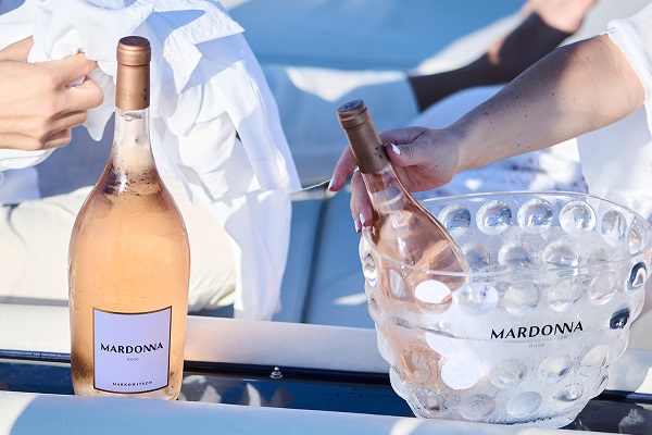 Mardonna_600x400 Eine Flasche Roséwein mit dem Etikett -MARDONA- steht neben einem gefrosteten Behälter. Eine Hand hält ein Glas, während eine andere Hand den Wein einschenkt. Der Hintergrund zeigt eine entspannte Outdoor-Umgebung.
