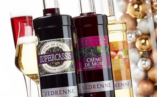 Drei Flaschen mit verschiedenen Likören stehen nebeneinander. Links befindet sich ein Glas mit schaumweinähnlichem Getränk. Im Hintergrund sind dekorative Elemente, möglicherweise Weihnachtsornamente, zu sehen.