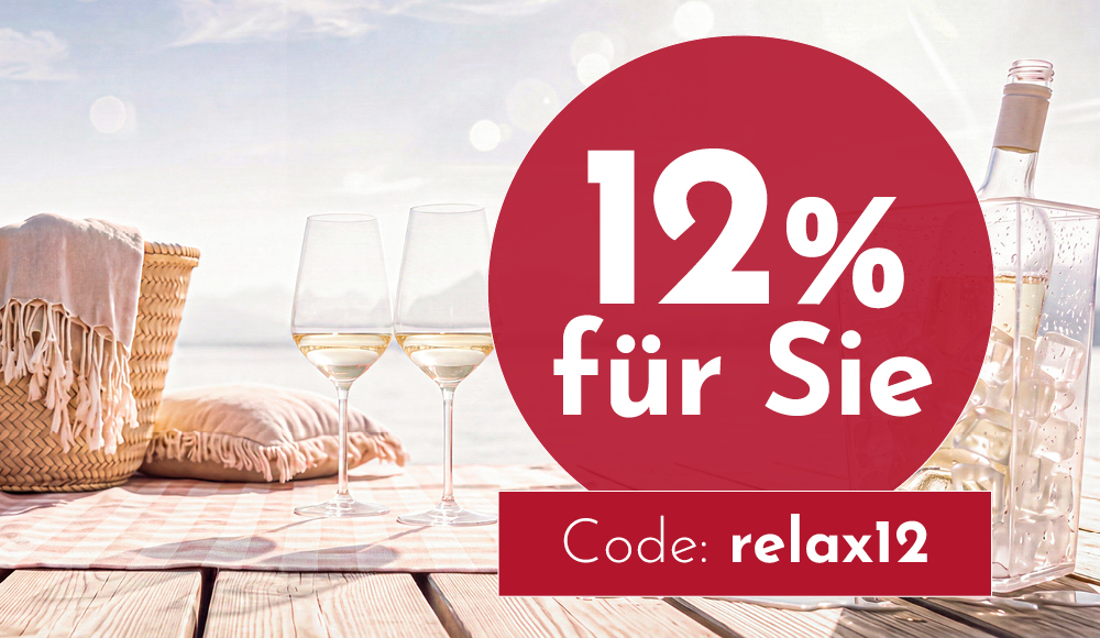 Zwei Weingläser stehen auf einer gestreiften Decke, umgeben von einem Korb und einem Kissen. Im Hintergrund ist Wasser und eine helle, sonnige Landschaft zu sehen. Text: -12% für Sie Code: relax12-.