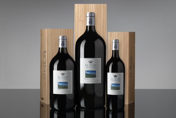 Drei Flaschen rotwein in verschiedenen Größen stehen nebeneinander auf einem spiegelnden Tisch. Sie sind in einer eleganten Präsentation mit hölzernen Kisten im Hintergrund angeordnet.