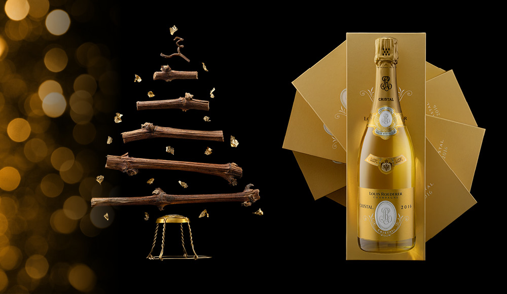 Ein stilisierter Weihnachtsbaum aus Holzstämmen ist im Vordergrund zu sehen, während goldene Funken umherfliegen. Rechts steht eine Flasche Louis Roederer Cristal 2016 in einer goldenen Verpackung.