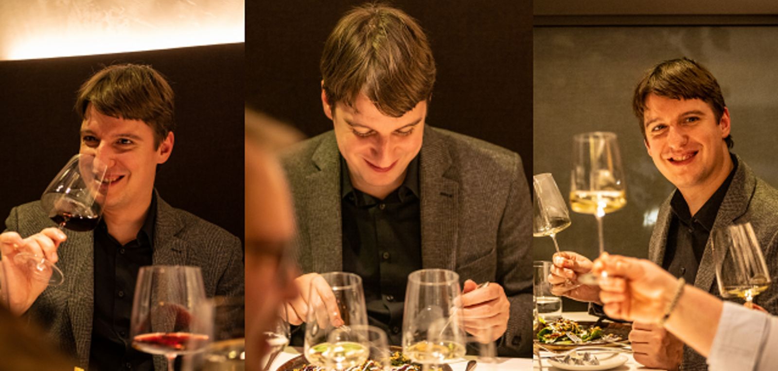 Ein Mann mit kurz geschnittenem Haar lächelt, während er ein Weinglas hält. Er sitzt an einem Tisch, umgeben von mehreren Weingläsern und einer Mahlzeit. Der Raum hat eine gedämpfte Beleuchtung.