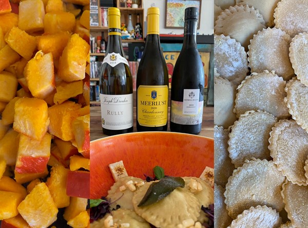 Würfelförmig geschnittenes Gemüse liegt auf einem Teller, daneben stehen drei Weinflaschen und eine große Schüssel mit einer cremigen Mischung, dekoriert mit Kräutern, sowie frische gefüllte Teigtaschen.