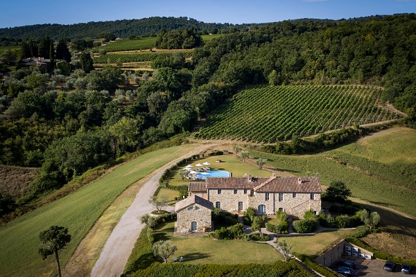 Ein landwirtschaftliches Anwesen aus Stein mit einem gefliesten Dach liegt umgeben von sanften Hügeln und Weinbergen. Im Vordergrund befindet sich ein gepflasterter Weg und ein Pool.