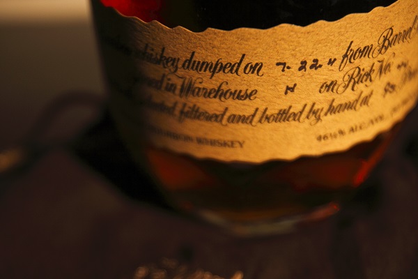 Ein Braunglas mit einer Etikette, auf der handgeschriebene Informationen über die Abfüllung des Whiskeys stehen. Der Hintergrund ist unscharf und dunkel.