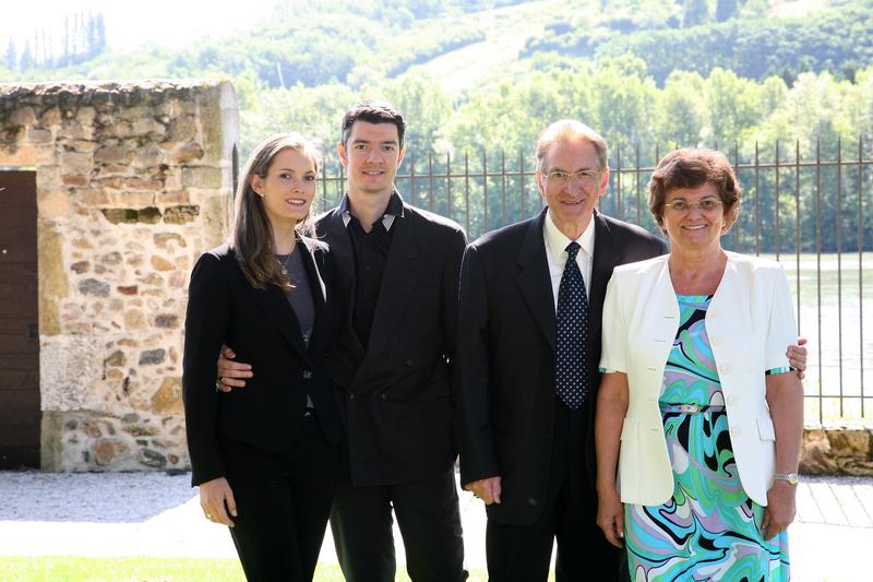 Vier Personen stehen zusammen, lächeln und posieren. Im Hintergrund sieht man eine flussnahe Landschaft mit Bäumen und sanften Hügeln. Es ist sonnig und die Atmosphäre wirkt freundlich.