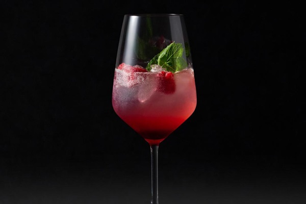 Ein elegantes Glas enthält einen erfrischenden Cocktail mit Eis, Himbeeren und einem Zweig Minze. Der Hintergrund ist schwarz, wodurch der Cocktail hervorhebt.