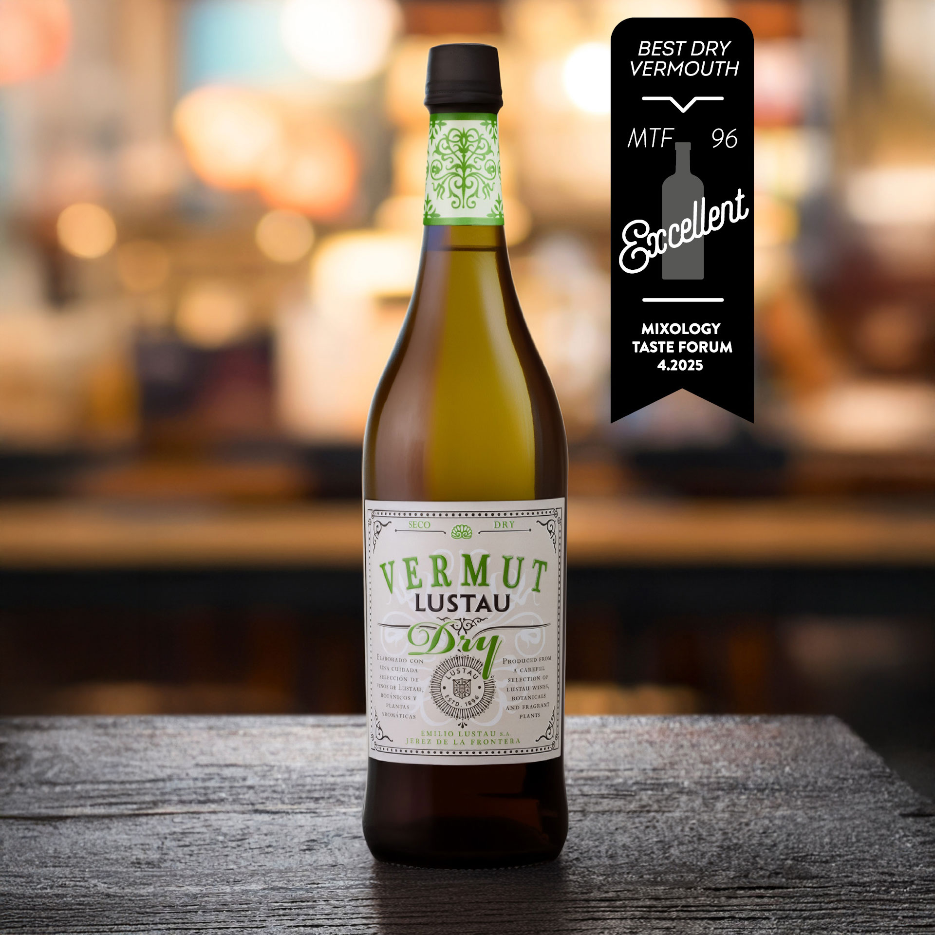 Eine Flasche Vermut Lustau steht auf einer Holzoberfläche. Die Flasche ist transparent mit einem elegant gestalteten Etikett, das die Worte -BEST DRY VERMOUTH- und -Exzellent- enthält, sowie eine Auszeichnung. Der Hintergrund zeigt eine unscharfe Bar-Umge