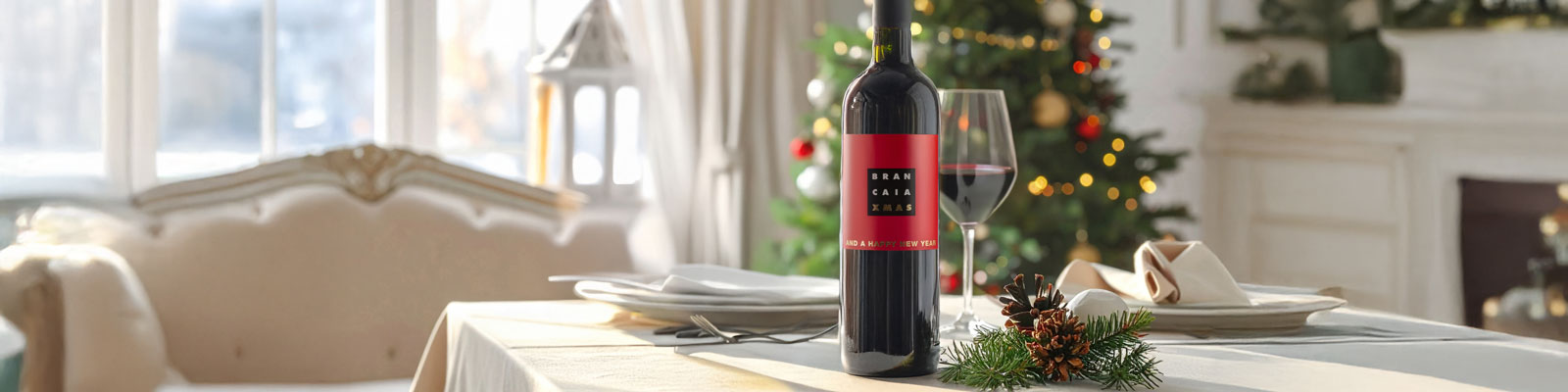 Eine elegante Flasche Rotwein steht auf einem festlich gedeckten Tisch, umgeben von einem Glas, Weihnachtsdekoration und einem geschmückten Baum im Hintergrund.