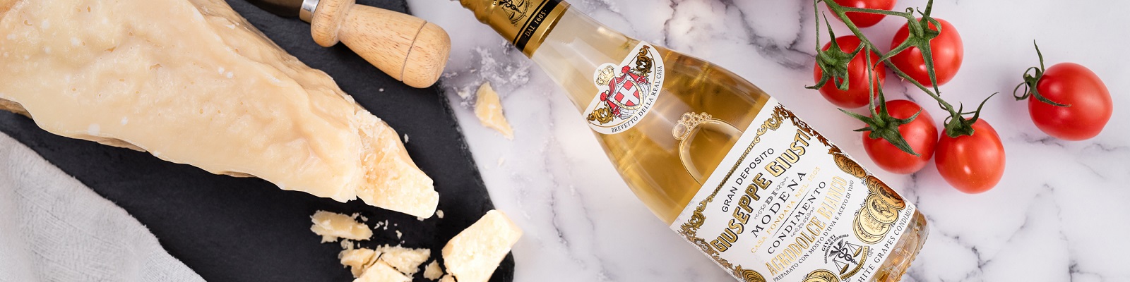 Ein Stück Parmesankäse liegt auf einem schwarzen Schneidebrett, daneben steht eine Flasche Balsamico-Essig und frische Kirschtomaten sind daneben gruppiert.