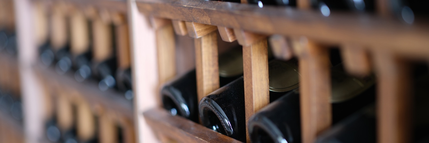 Ein Weinständer aus Holz mit diagonal angeordneten Fächern, in denen zahlreiche Weinflaschen liegen. Die Flaschen sind schwarz und teils gut sichtbar, während einige versteckt sind.