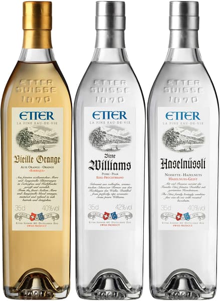 Obstbrand Topseller Vorteilspaket Drei Flaschen Obstbrände stehen nebeneinander. Links eine goldene Flasche mit der Aufschrift -Vieille Orange-, in der Mitte eine klare Flasche mit -Birne Williams- und rechts eine klare Flasche mit -Haselnüssli-.